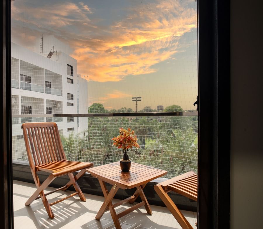 Hotel room balcony with wooden chairs and a table overlooking the surrounding area at sunset at Arawali Ananta Elite, Jaipur.