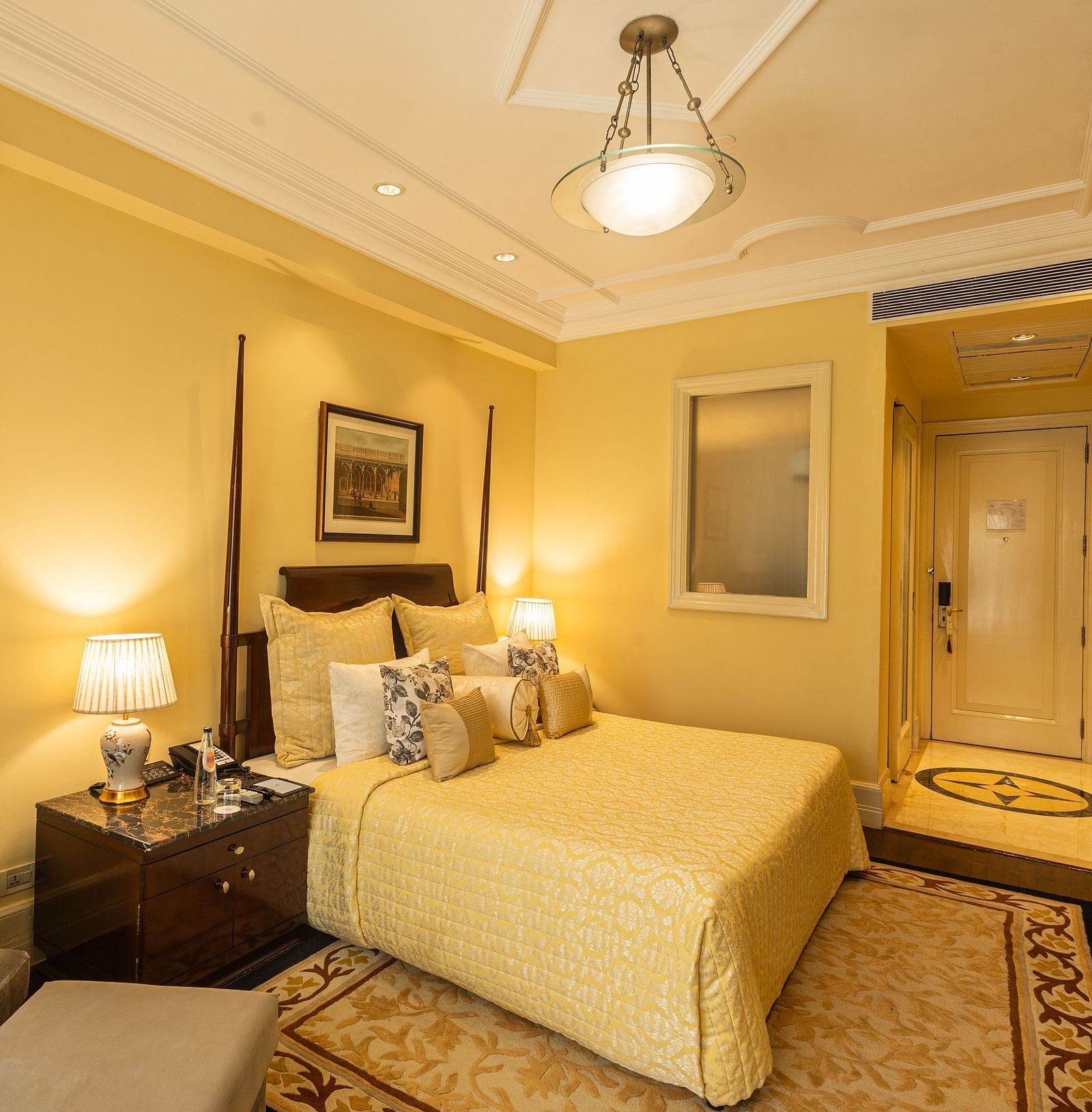 Side view of the Deluxe King Bed Room Pool View at The Claridges New Delhi, featuring a cosy king sized bed, wall-mounted TV, and bedside lamps