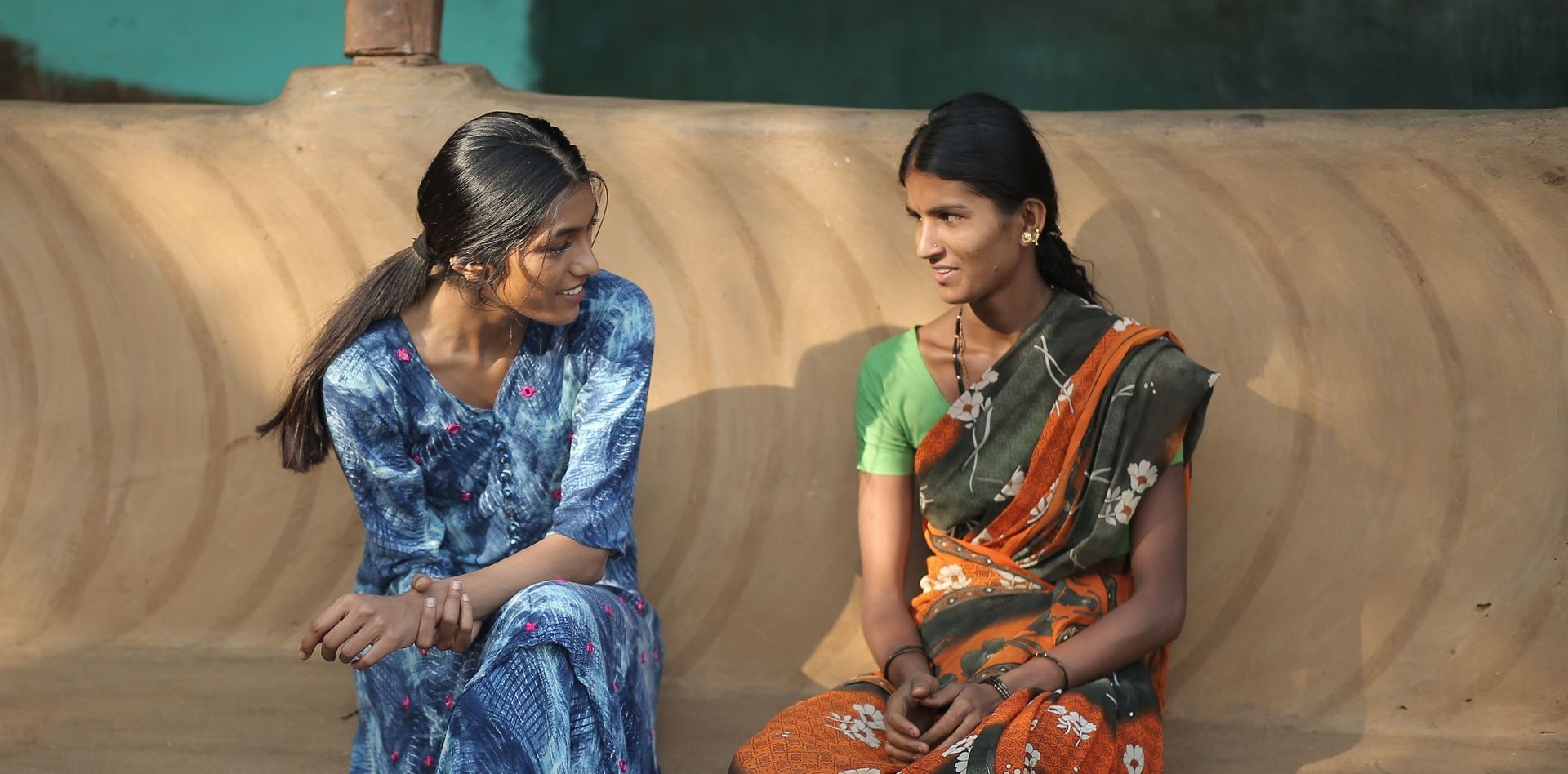 Two women in traditional Indian attire, rural setting.