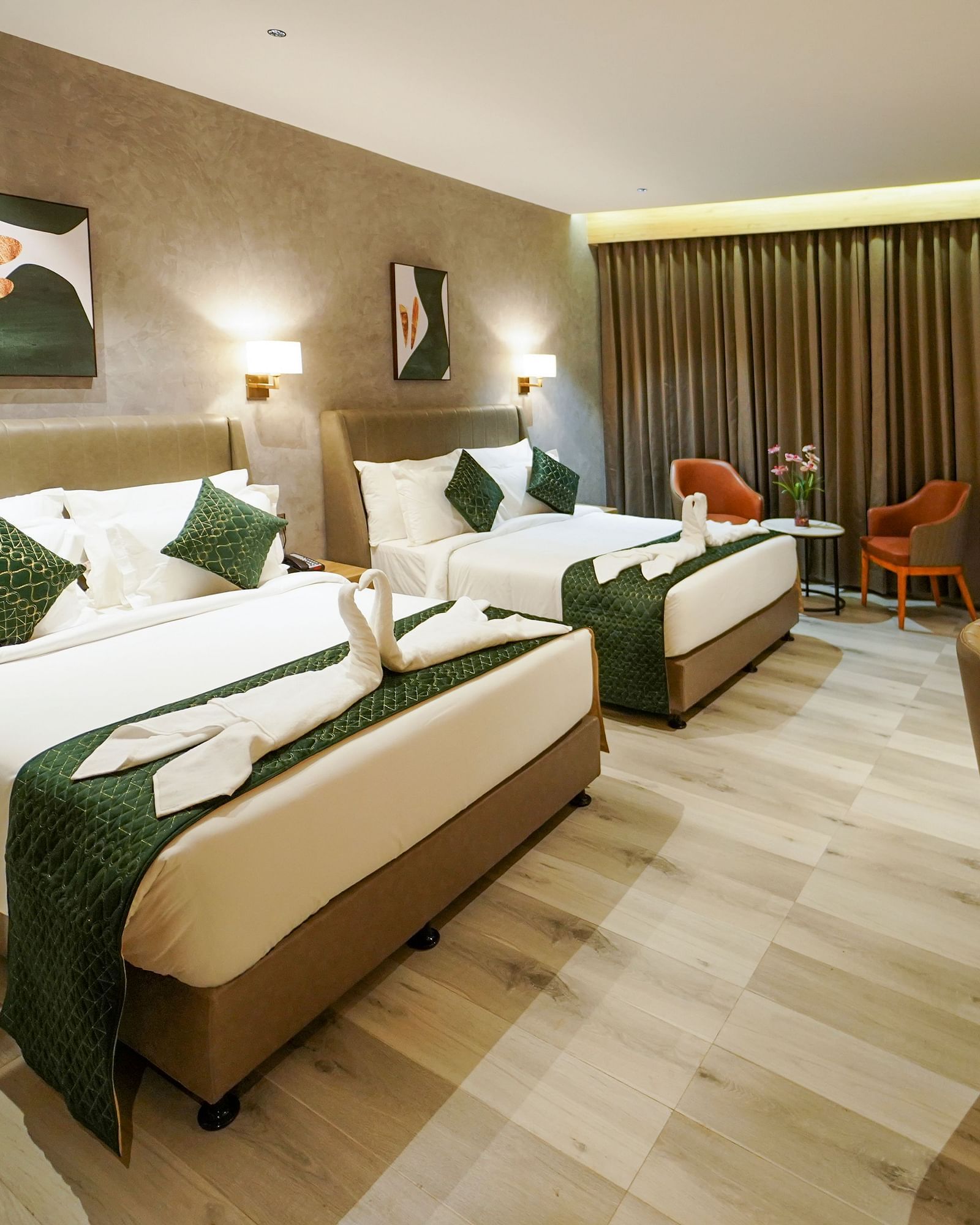 A hotel room features two beds with decorative towels and pillows, a desk with a lamp, and a seating area with a small table - Hotel Park Inn, Nellore.