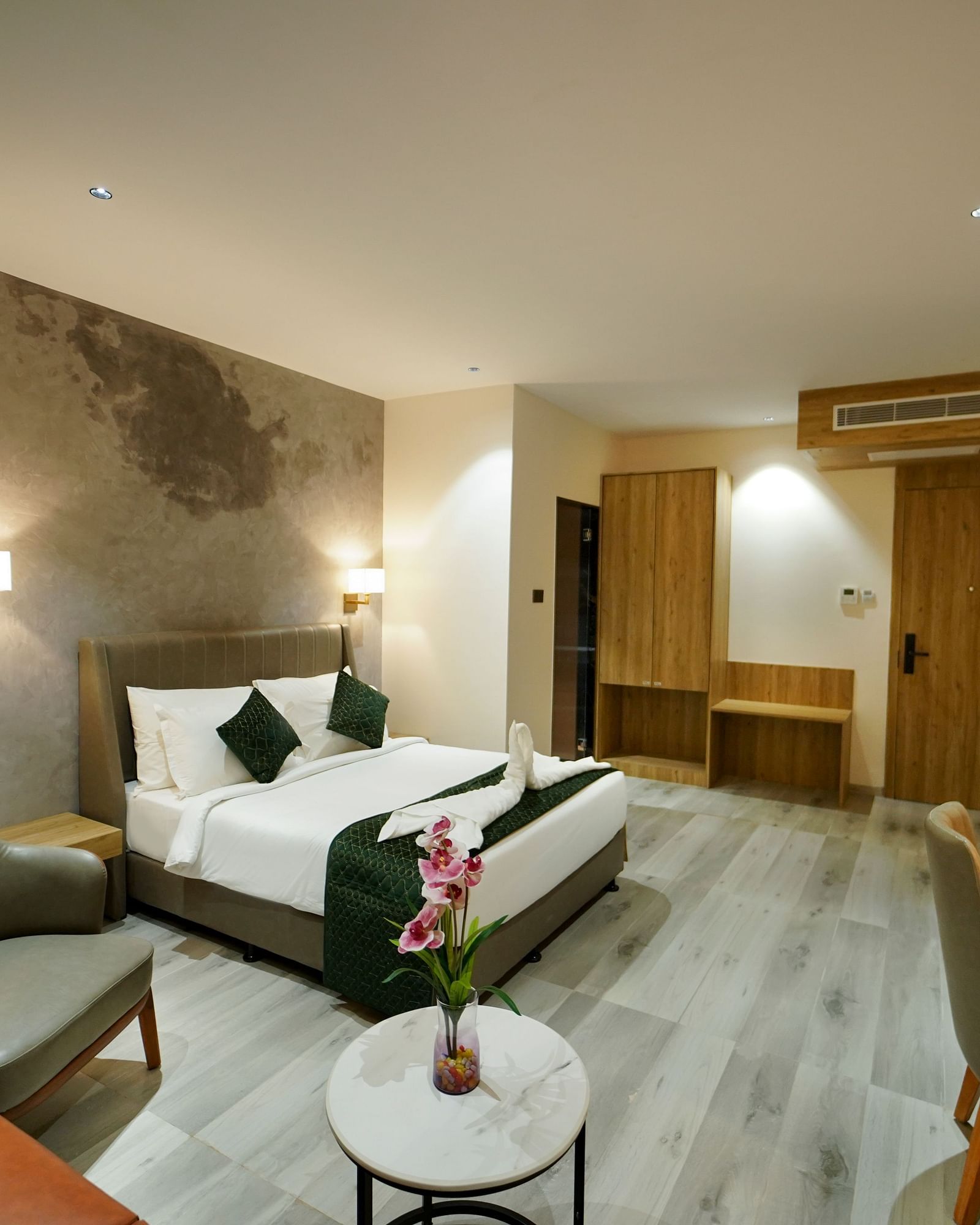 3A hotel room features a bed with pillows and a throw, a seating area with a small table and flowers, and a desk with a lamp. - Hotel Park Inn, Nellore.