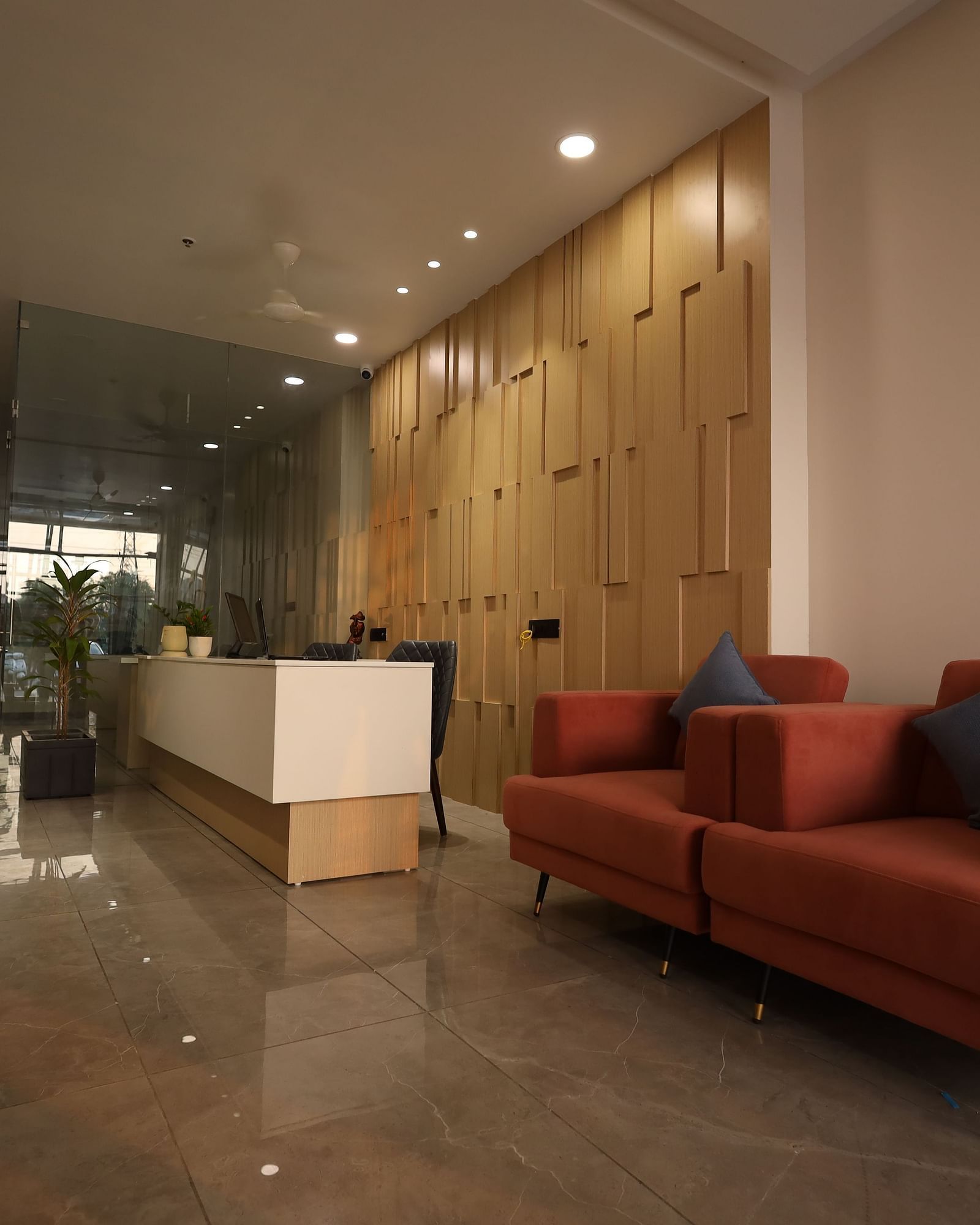 The image shows a reception or waiting area with sofas, a front desk, and a potted plant - Lords Eco Inn Navsari.