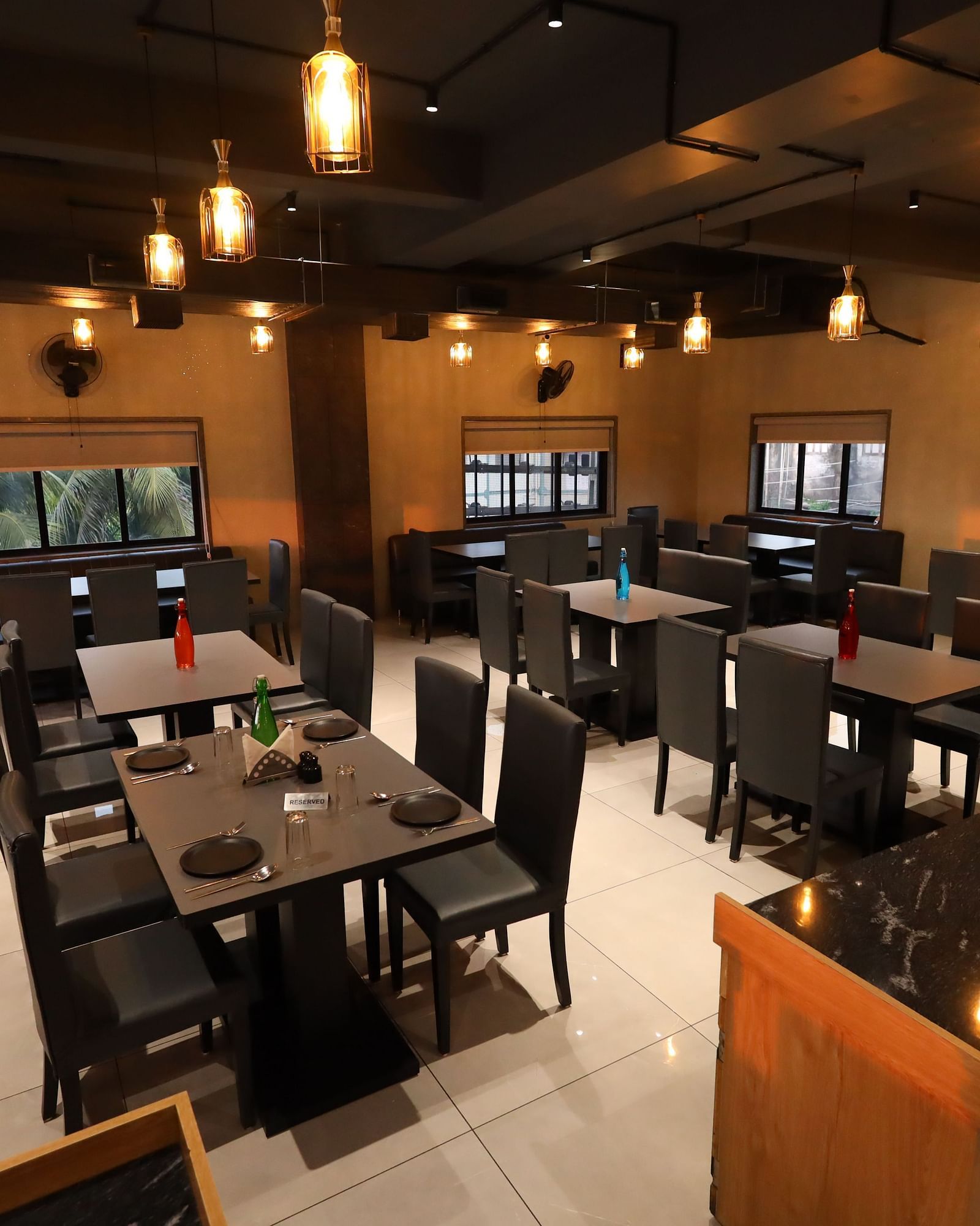 The image depicts a restaurant interior with set tables and chairs under warm, hanging lights - Lords Eco Inn Navsari.