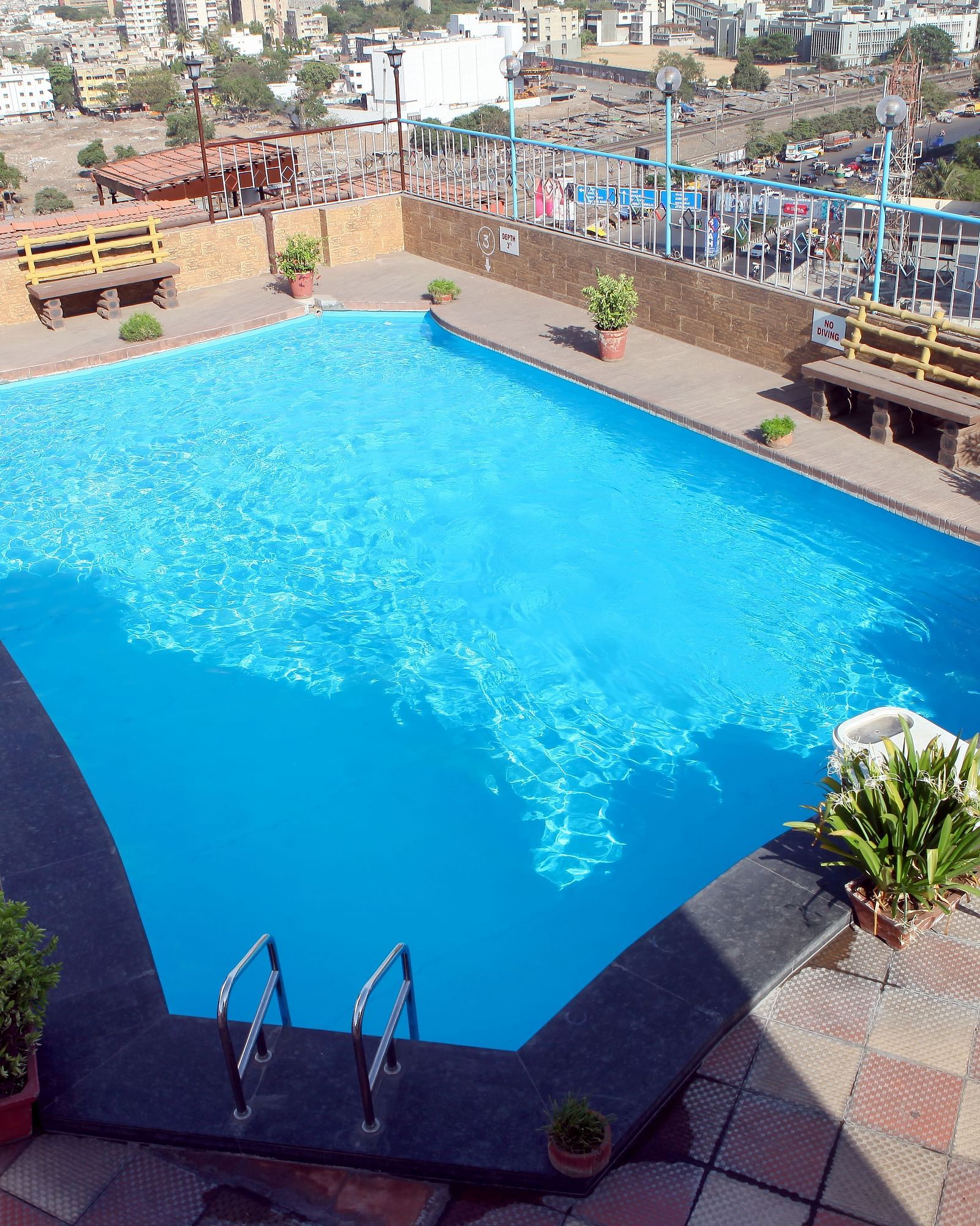 An outdoor swimming pool with surrounding cityscape at Lords Plaza Surat.