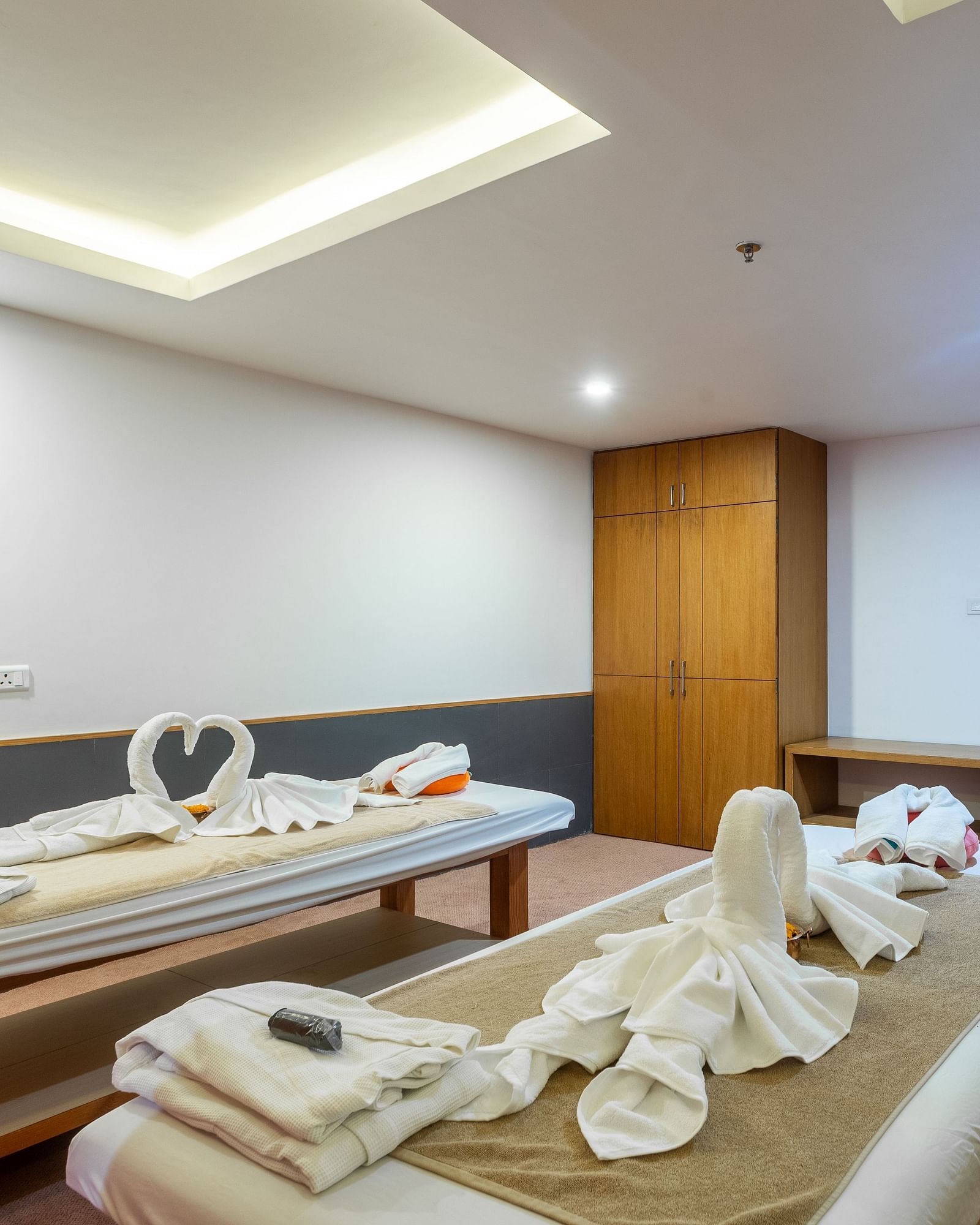 Two spa tables placed in a room with carpeted flooring, curtained windows, a chair and a table at Mandala Norling Lords Prime in Kathmandu.