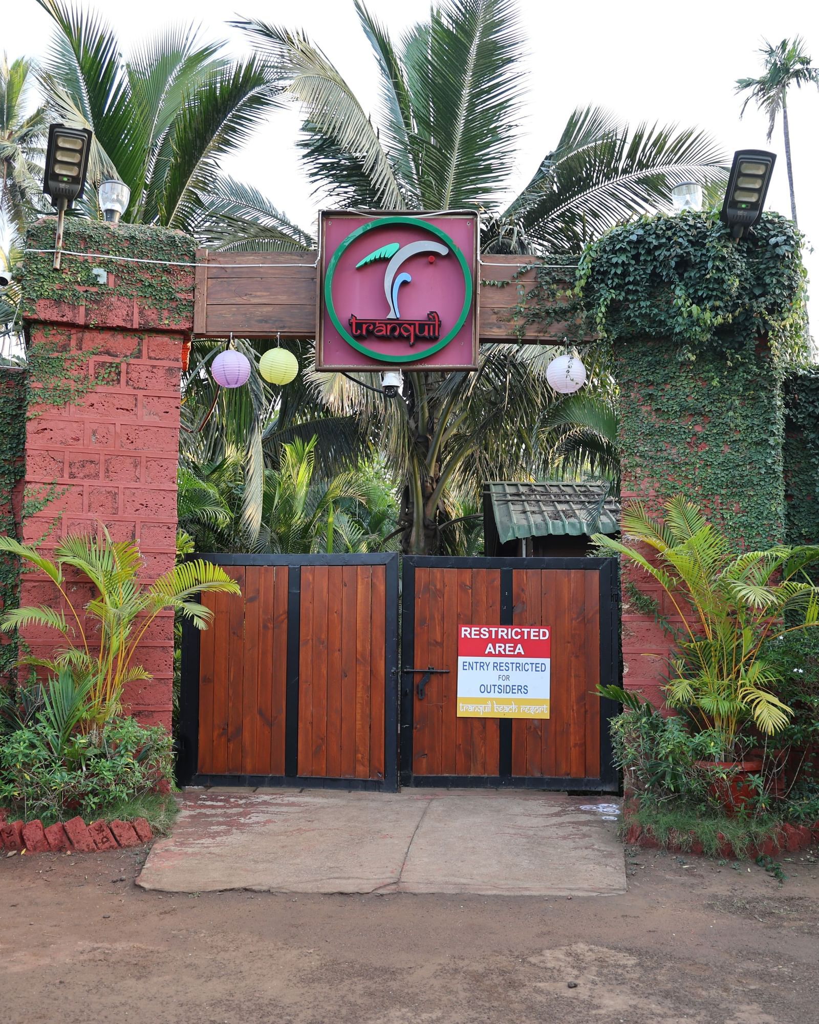 Ornate resort entrance gate made of stone and wood, surrounded by lush green foliage - Tranquil Beach Resort, Harihareshwar