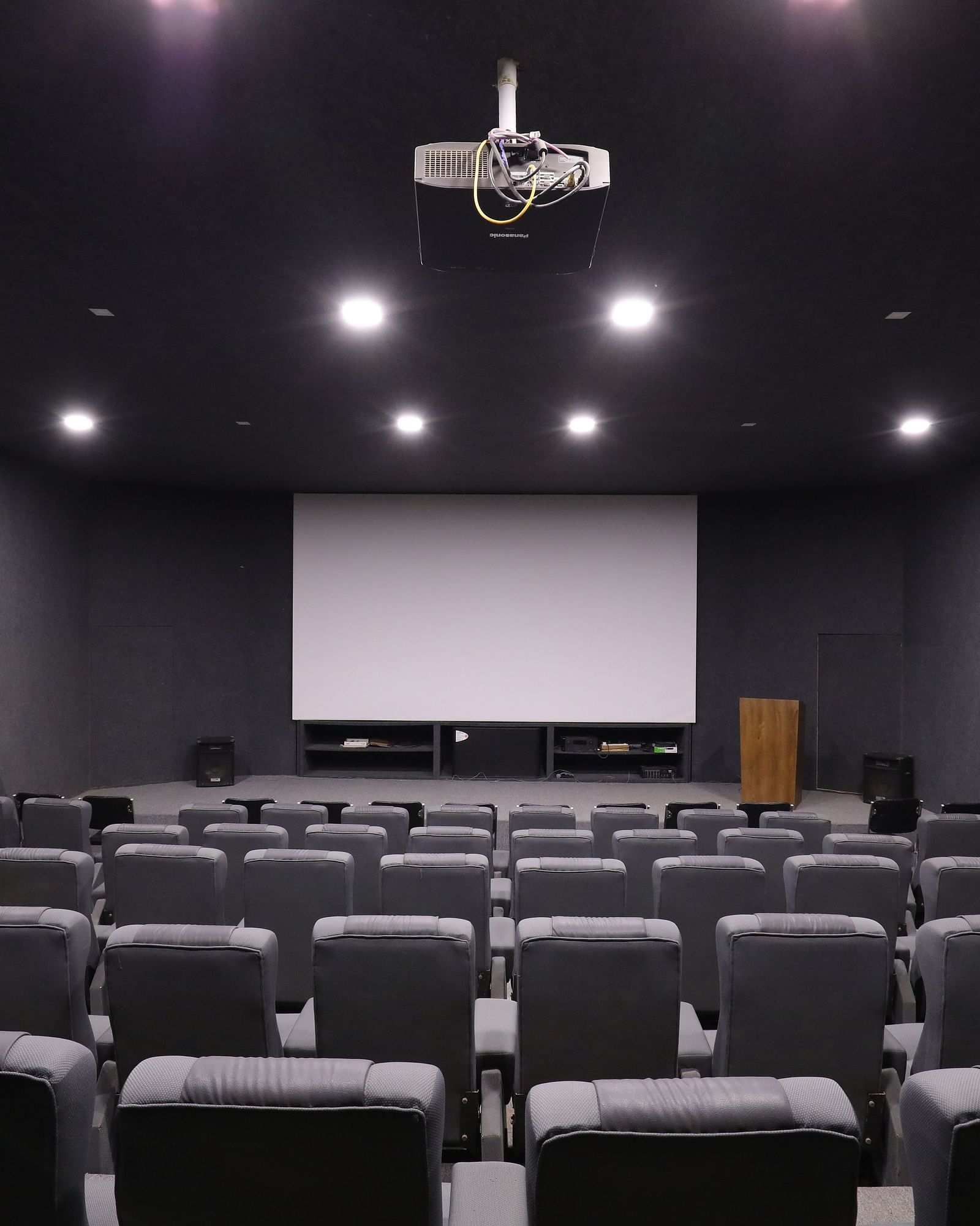A private cinema room with rows of plush seating facing a large projection screen - Vishal Lords Inn Gir Forest