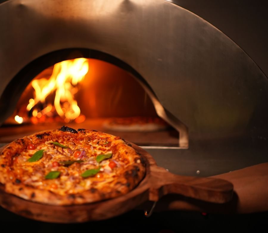 Close up of a wood fire pizza near a wood fire oven featuring it's delicious loaded cheese and veggies at Rangamati Garden Resort.