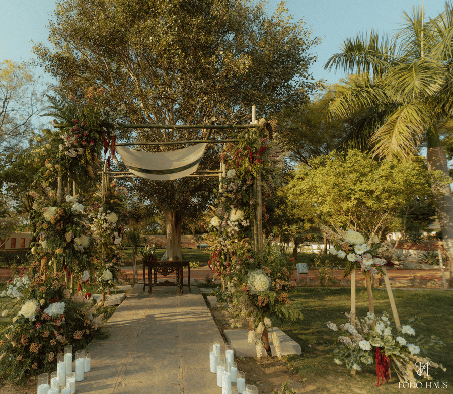 An outdoor wedding altar decorated with lush greenery and white flowers on a lawn at Umaid Palace.