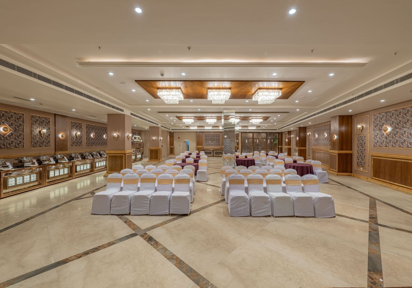 Large banquet hall at Hotel Highway King, Bagru, with rows of chairs, decorative ceiling lights, and mirrored wall panels.