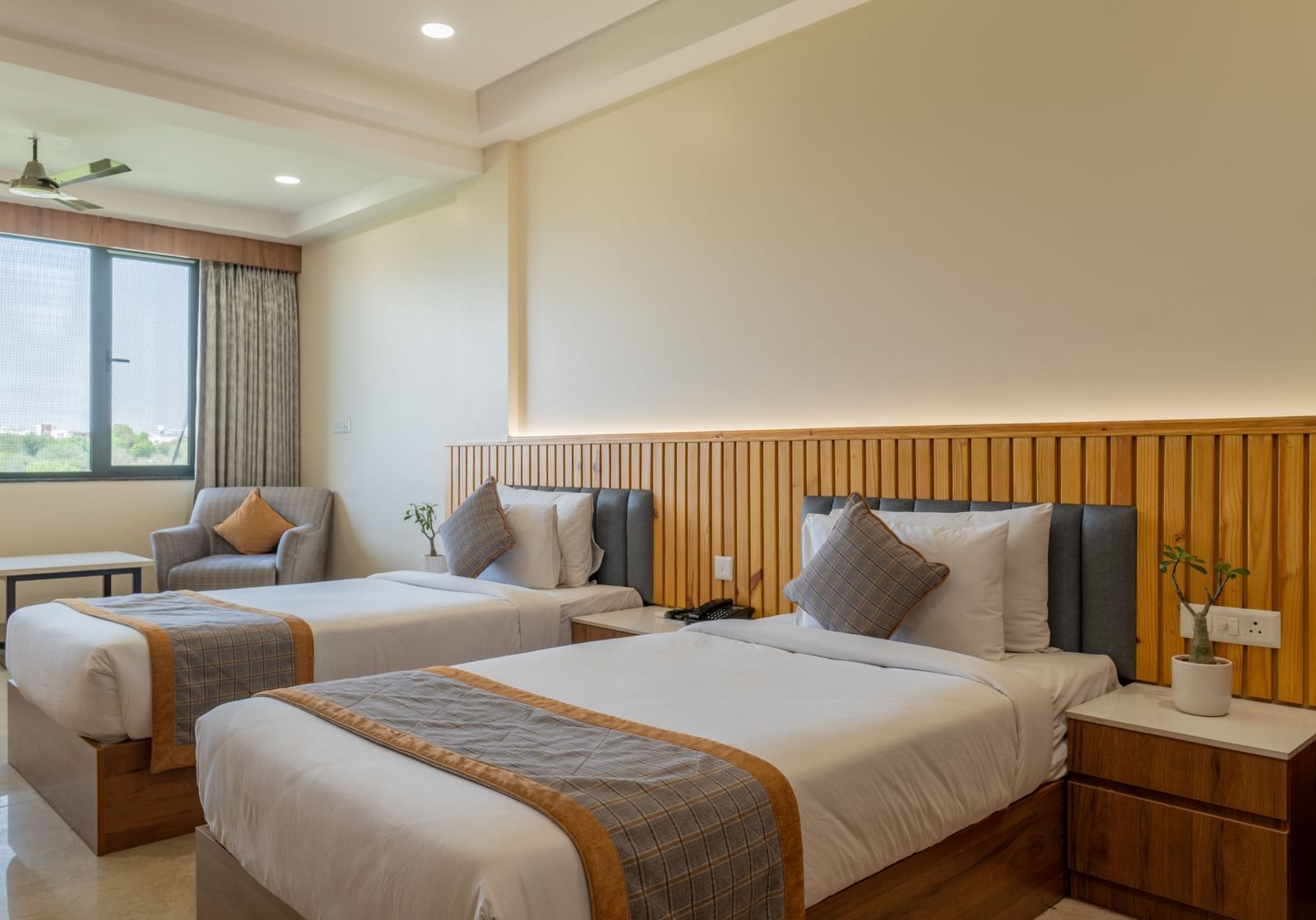 Twin bedroom at Hotel Highway King, Bagru, with bedside tables, large window, and upholstered headboards.