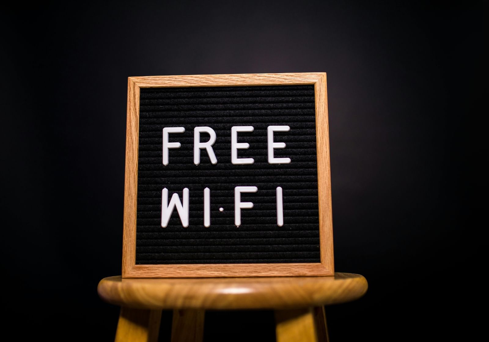 Letter board on wooden stool displaying the words Free WiFi in white letters against a black background.