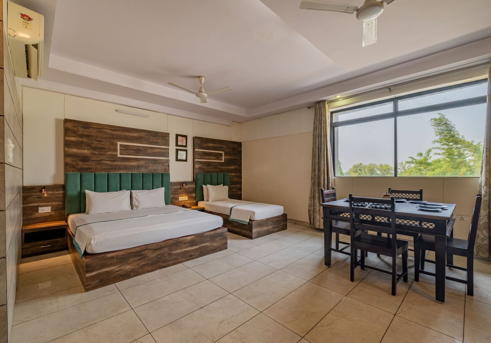 Extended view of the double and single bed, dining table and open glass windows in the Suite of Hotel Highway King in Behror.