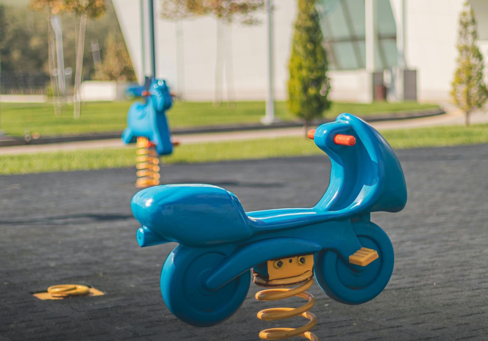 A vibrant spring toy set up in a spacious play area with lawn patches and trees in the blurry background.