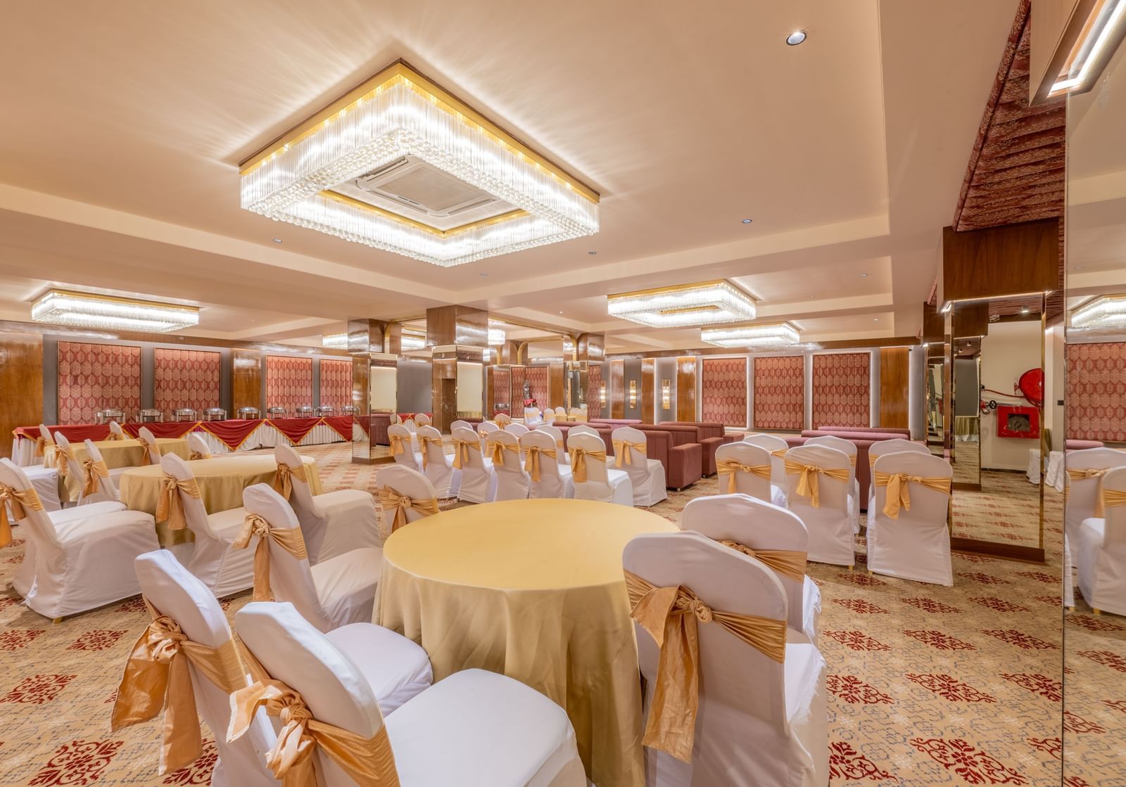 Round tables with yellow tablecloths and white chairs arranged under a decorative ceiling light at Hotel Highway King, Jaipur.