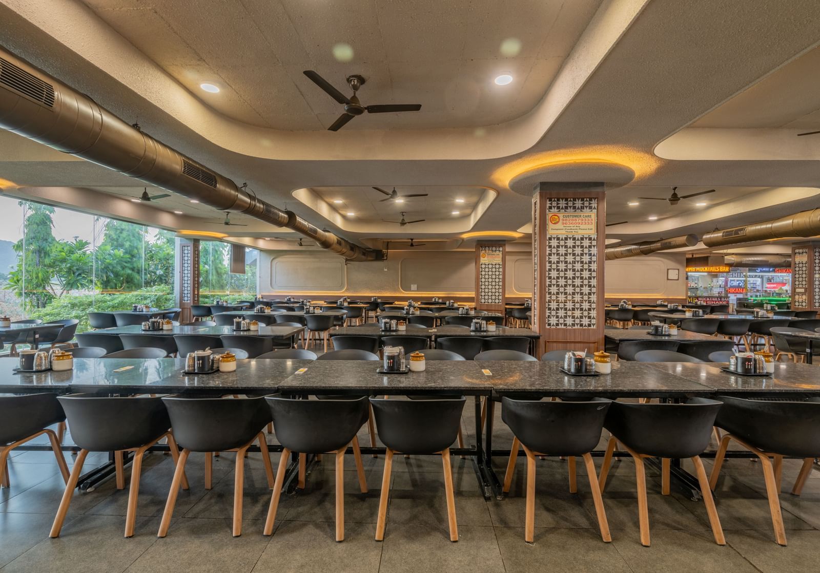 Chairs neatly arranged around a table with a glass panel to the side, offering a view of the lawn at Hotel Highway King, Neelka.