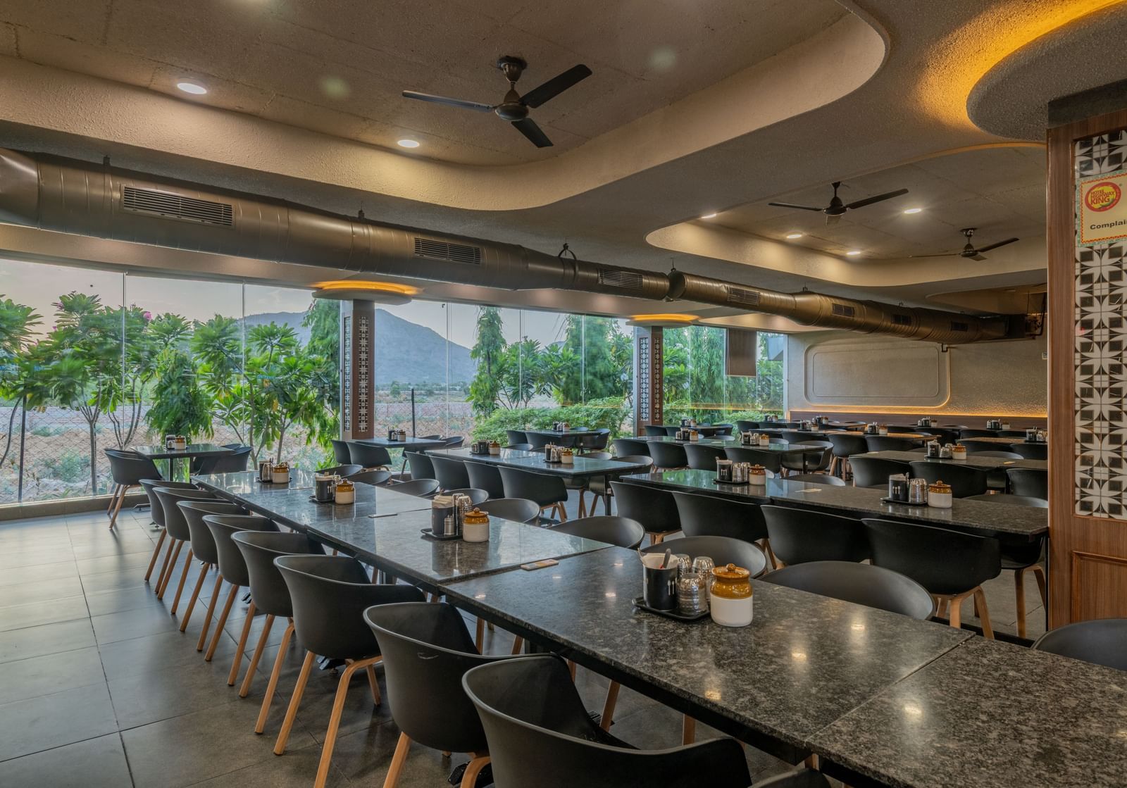 Spacious, modern dining area with black chairs, large windows, and ambient lighting at Hotel Highway King, Neelka.