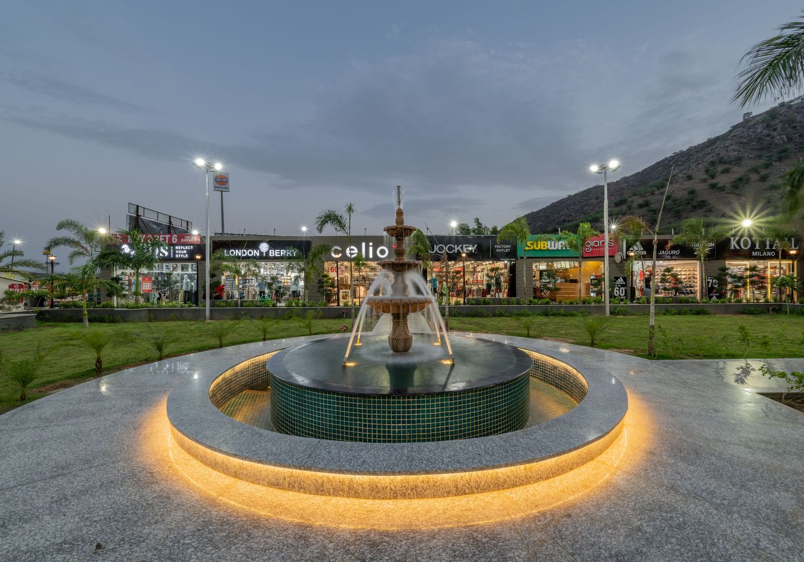 Close-up view of the fountain against the evening sky with a shopping complex in the background at Hotel Highway King, Neelka.