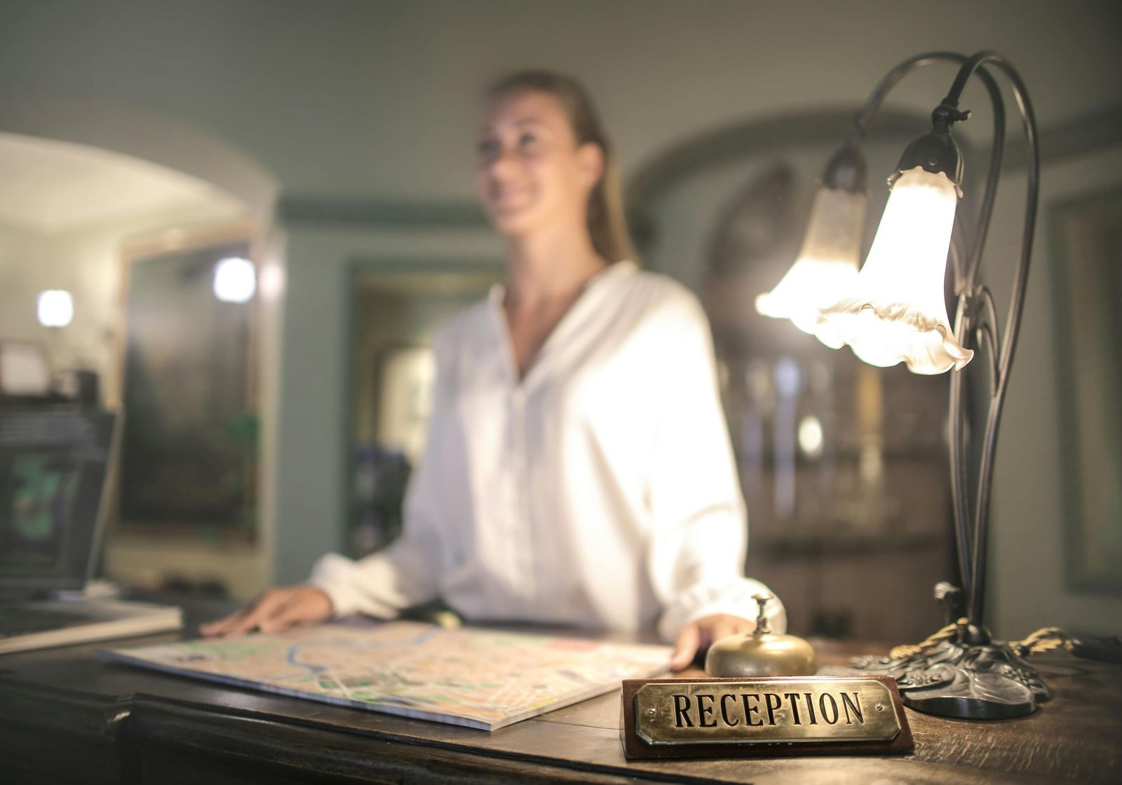 A hotel receptionist standing at the front desk with a glowing lamp.