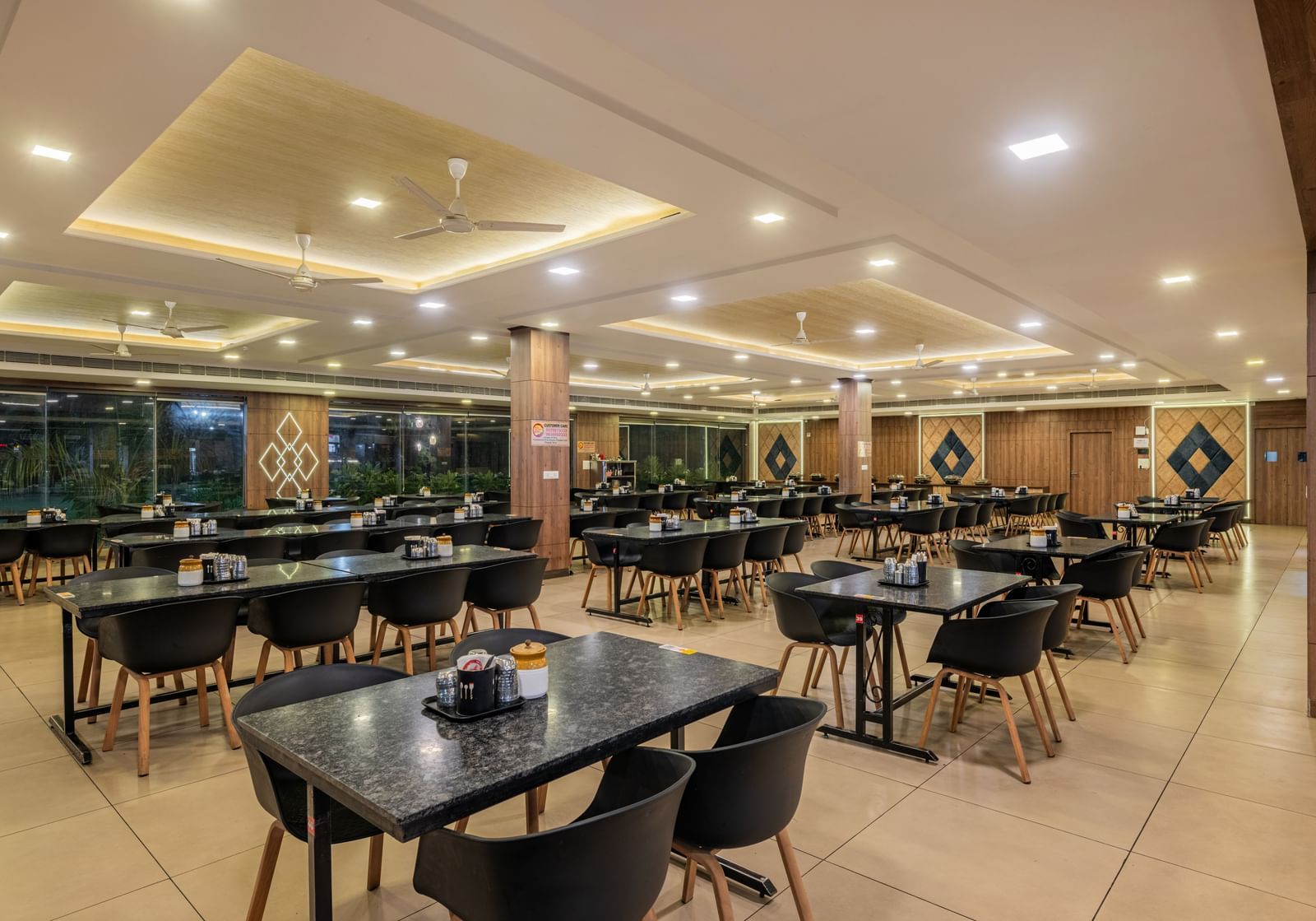 An empty, well-lit dining area inside the Hotel Highway King Shahpura, set with numerous tables and chairs.