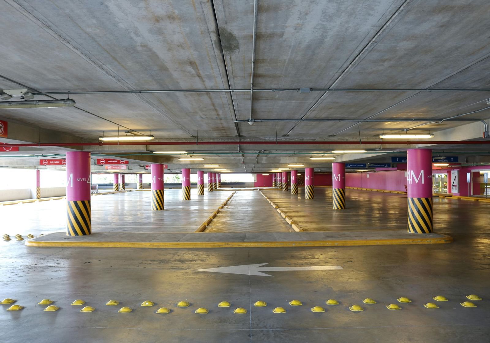 A wide, empty underground parking garage with concrete ceilings, support pillars, and painted markings on the floor.