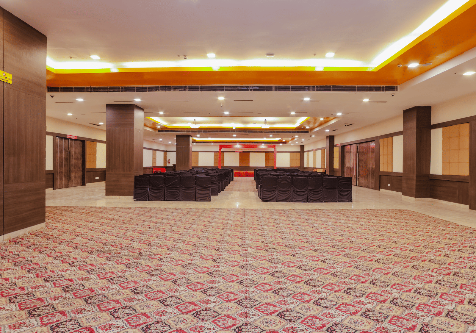 A large, empty ballroom or banquet hall with a patterned carpet, high ceilings, and a stage or raised platform at the far end, ready for an event.