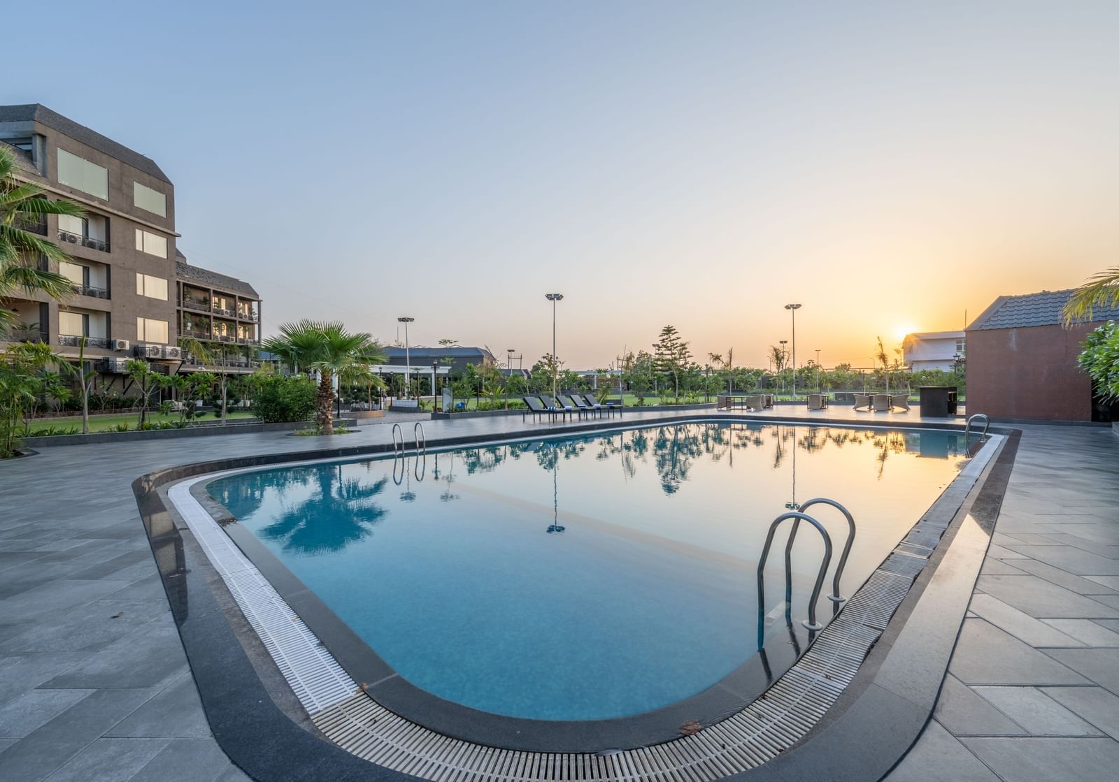 Swimming pool area at Hotel Highway King, Bagru, with loungers, landscaped garden, and hotel building.