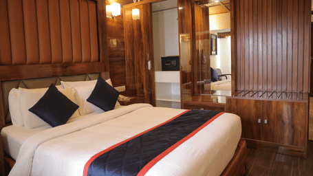 A spacious hotel suite with a large double bed, wooden panelling, and mirrored wardrobe doors - Benzz Park, Kodaikanal