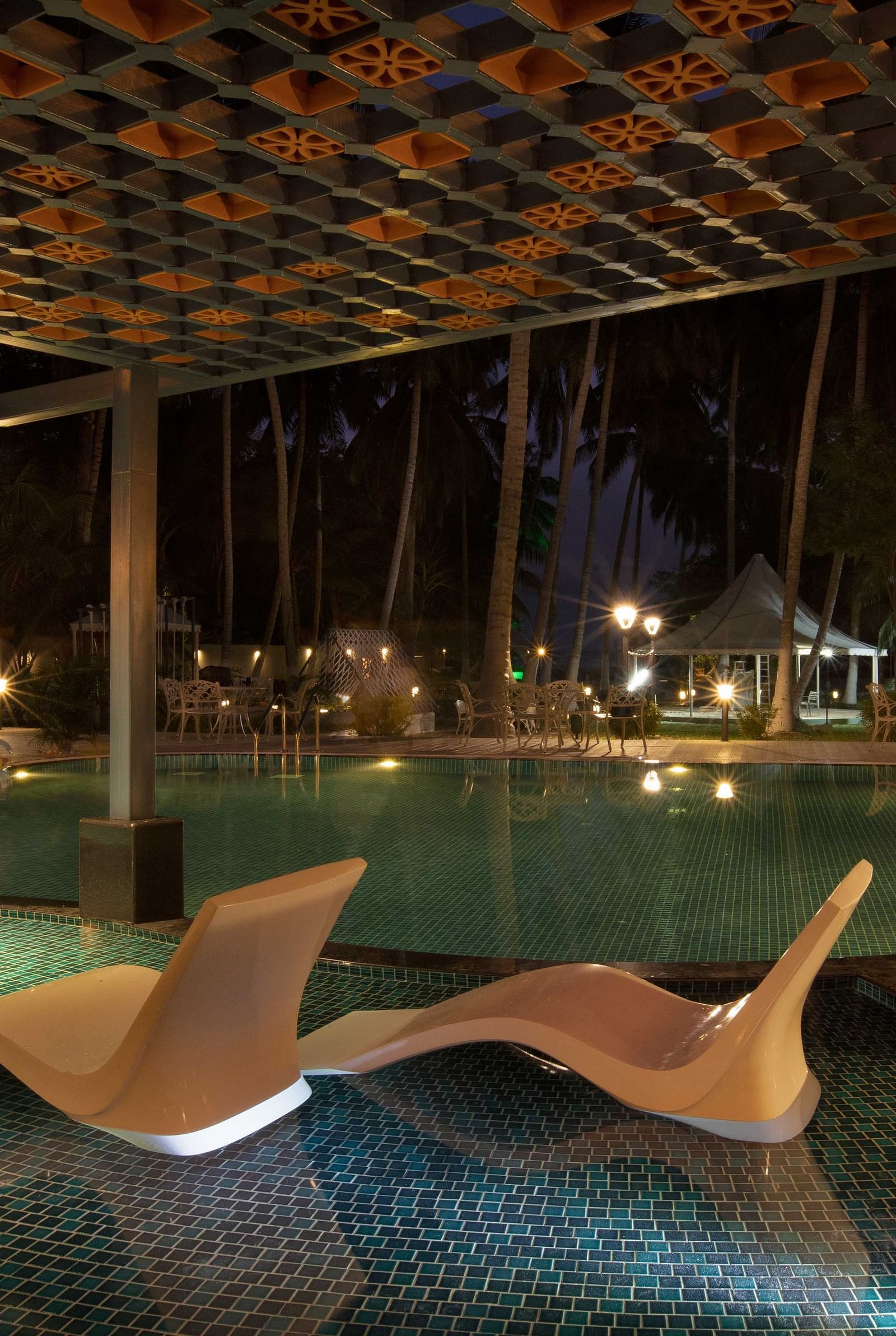 A tranquil outdoor pool area at dusk, with illuminated seating areas and palm trees surrounding the pool. The space has a peaceful, tropical atmosphere - Coral Reef Resort & Spa, Havelock