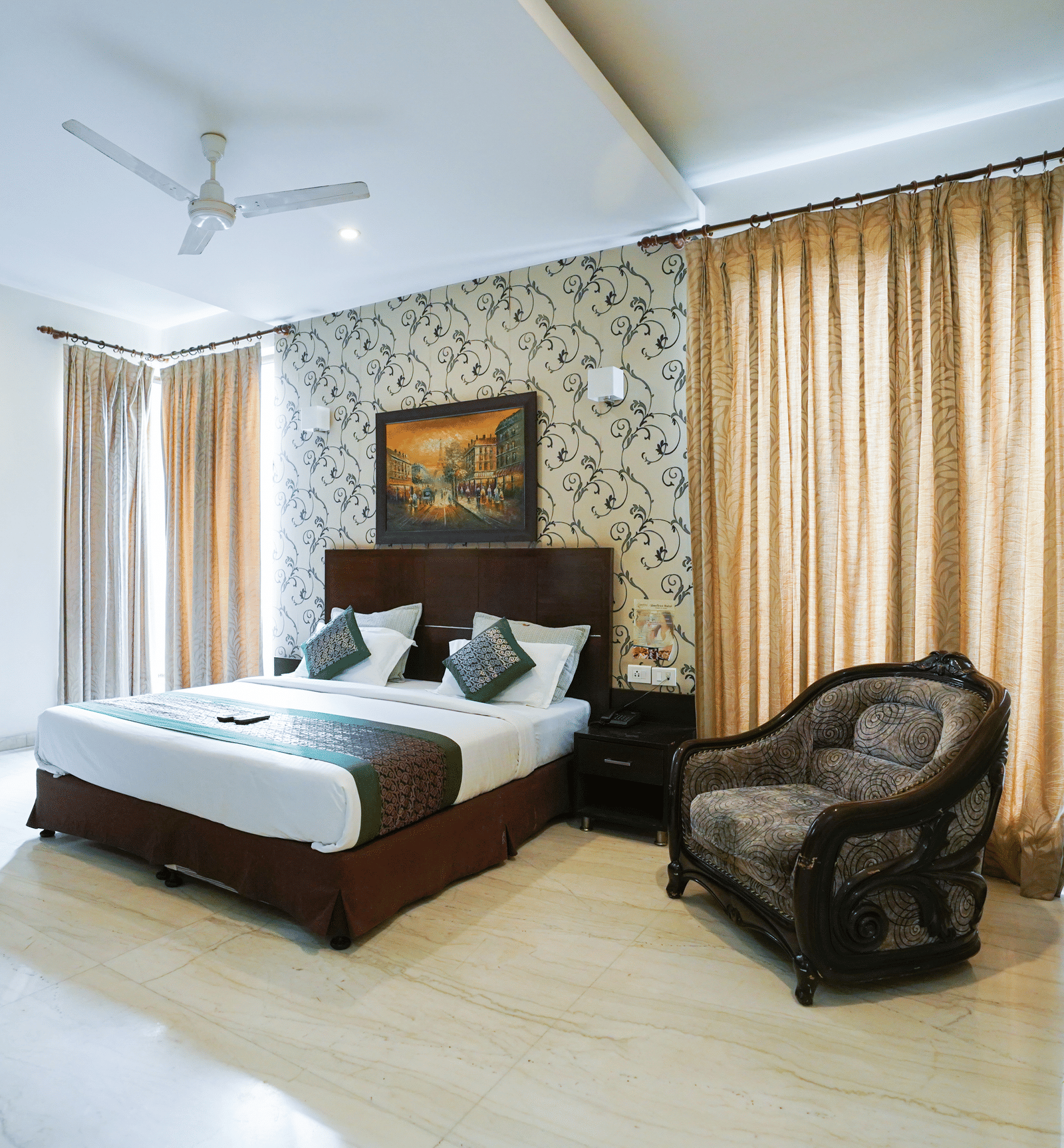 The king size bed, upholstered chair, and drawn curtains in the spacious Deluxe Room With Balcony of Lime Tree Hotel, IFFCO Chowk.