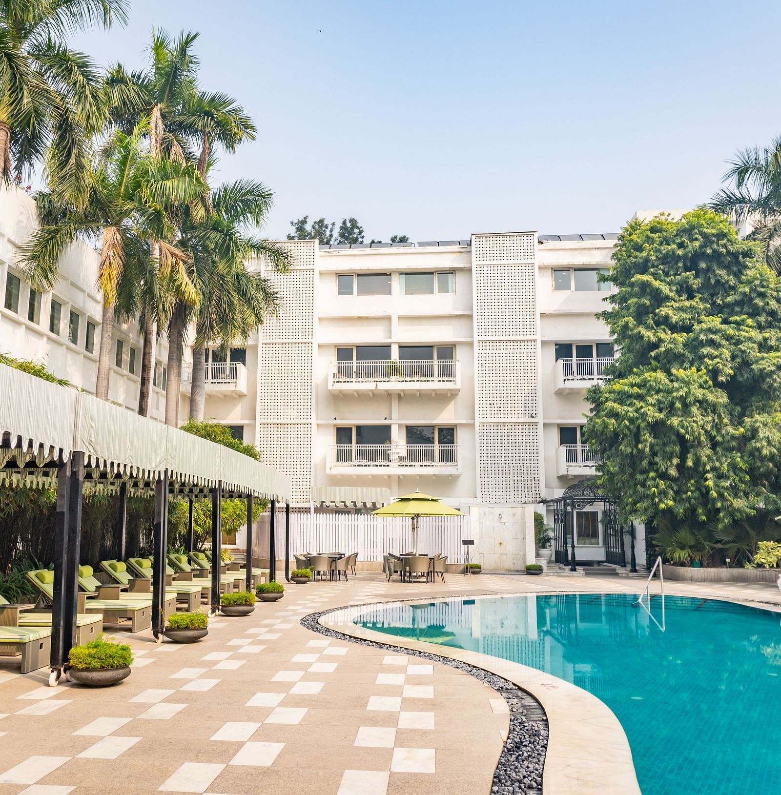 a bright facade image of The Claridges New Delhi with glittering blue swimming pool with green sunloungers