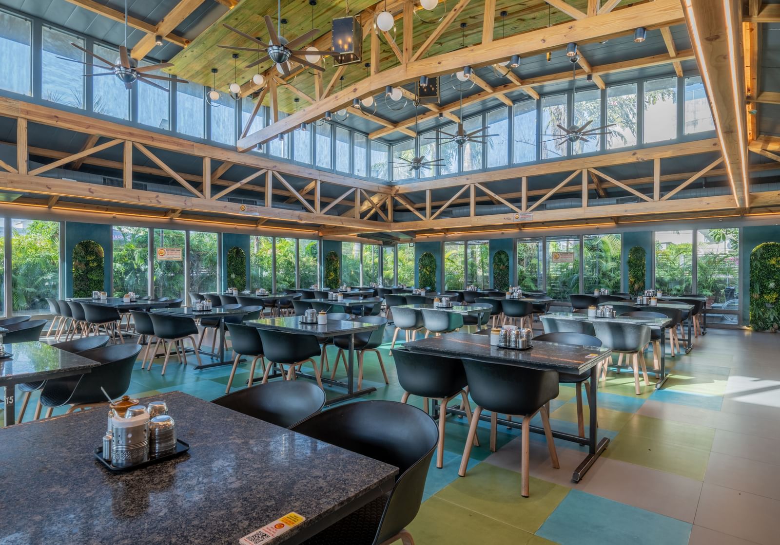 Spacious dining hall with black tables, wooden rafters, and full-length windows at Hotel Highway King, Jaipur.