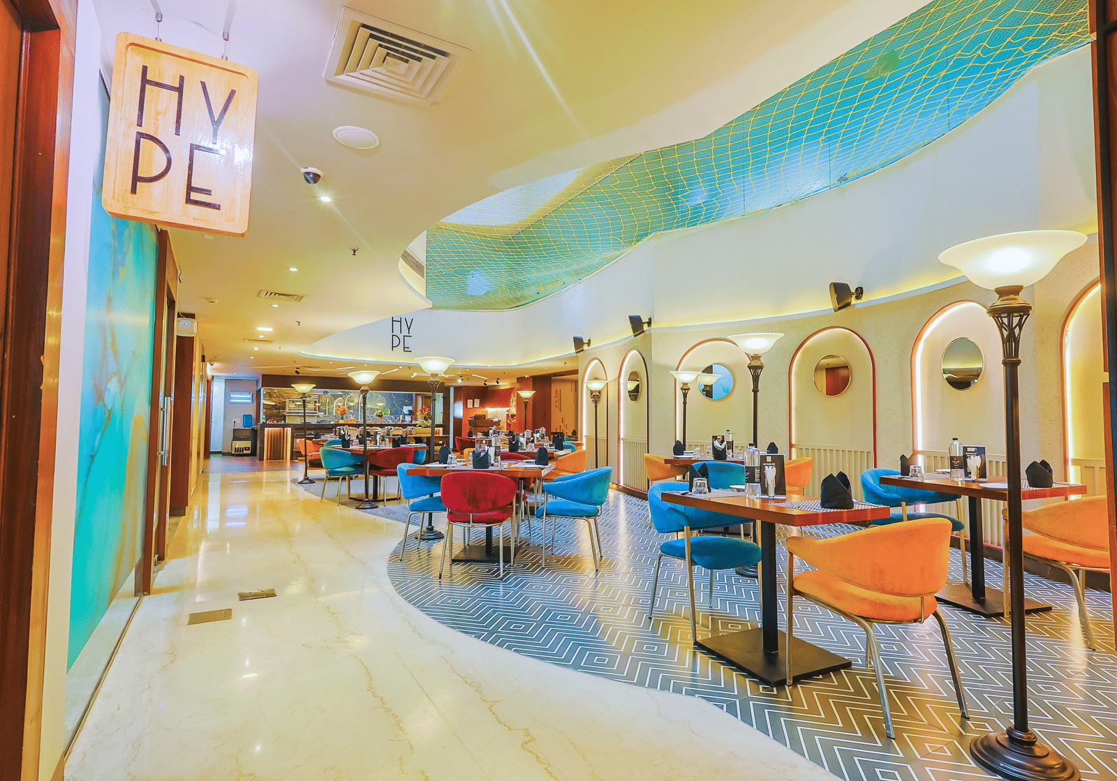 A contemporary restaurant or cafe interior with colourful seating, varied table sizes, and bright lighting, creating an inviting atmosphere.