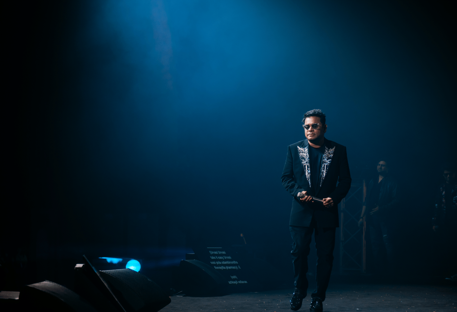 A. R. Rahman performing live on stage under blue lighting.