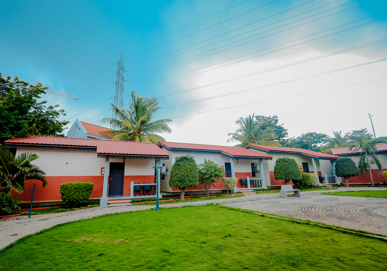 Exterior view of cottages with red roofs and green lawns at Nirantara Resort & Spa, Bengaluru, under a partly cloudy sky.