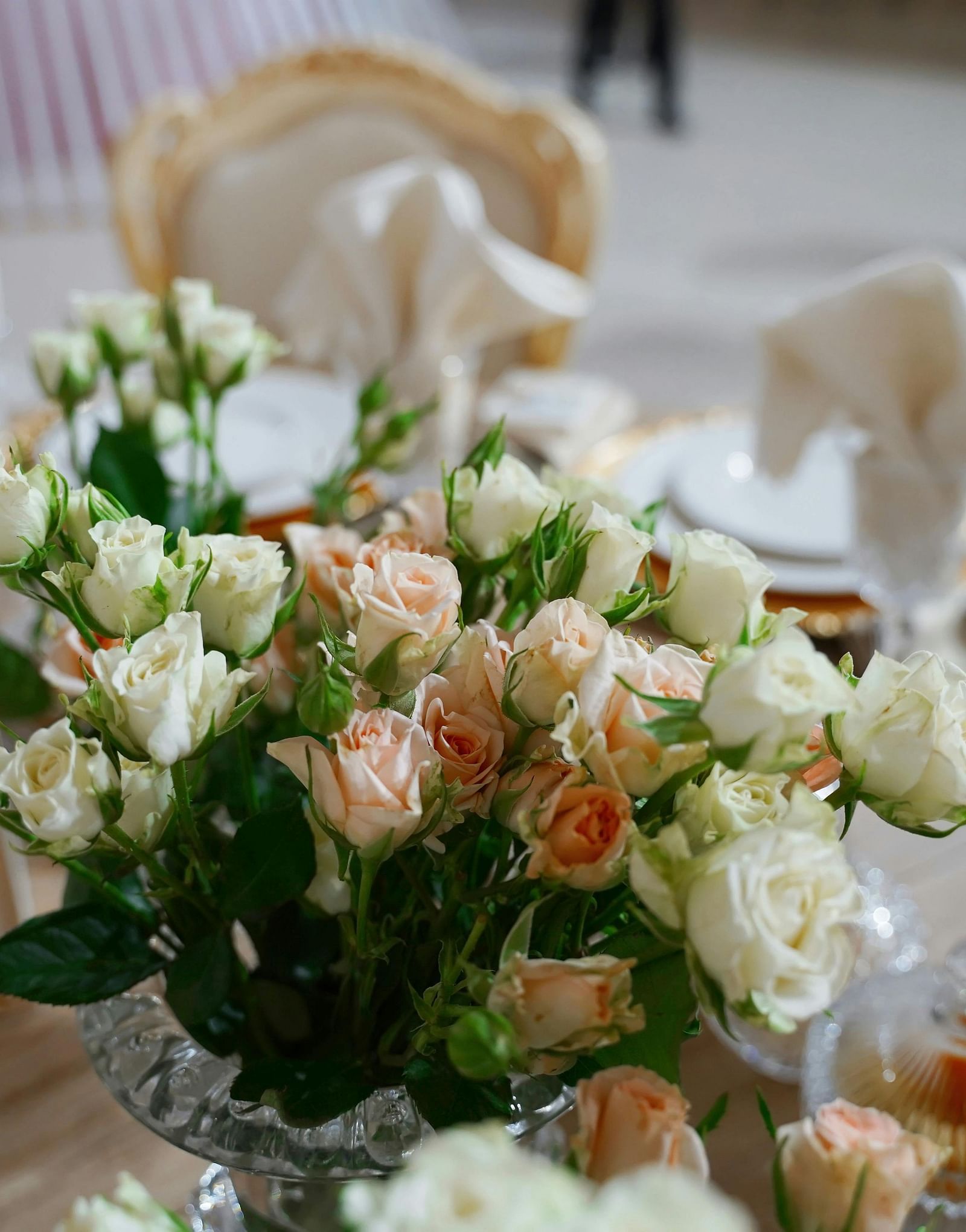 A close up shot of a beautiful flower vase with a lot of white and pink roses on a dining table.
