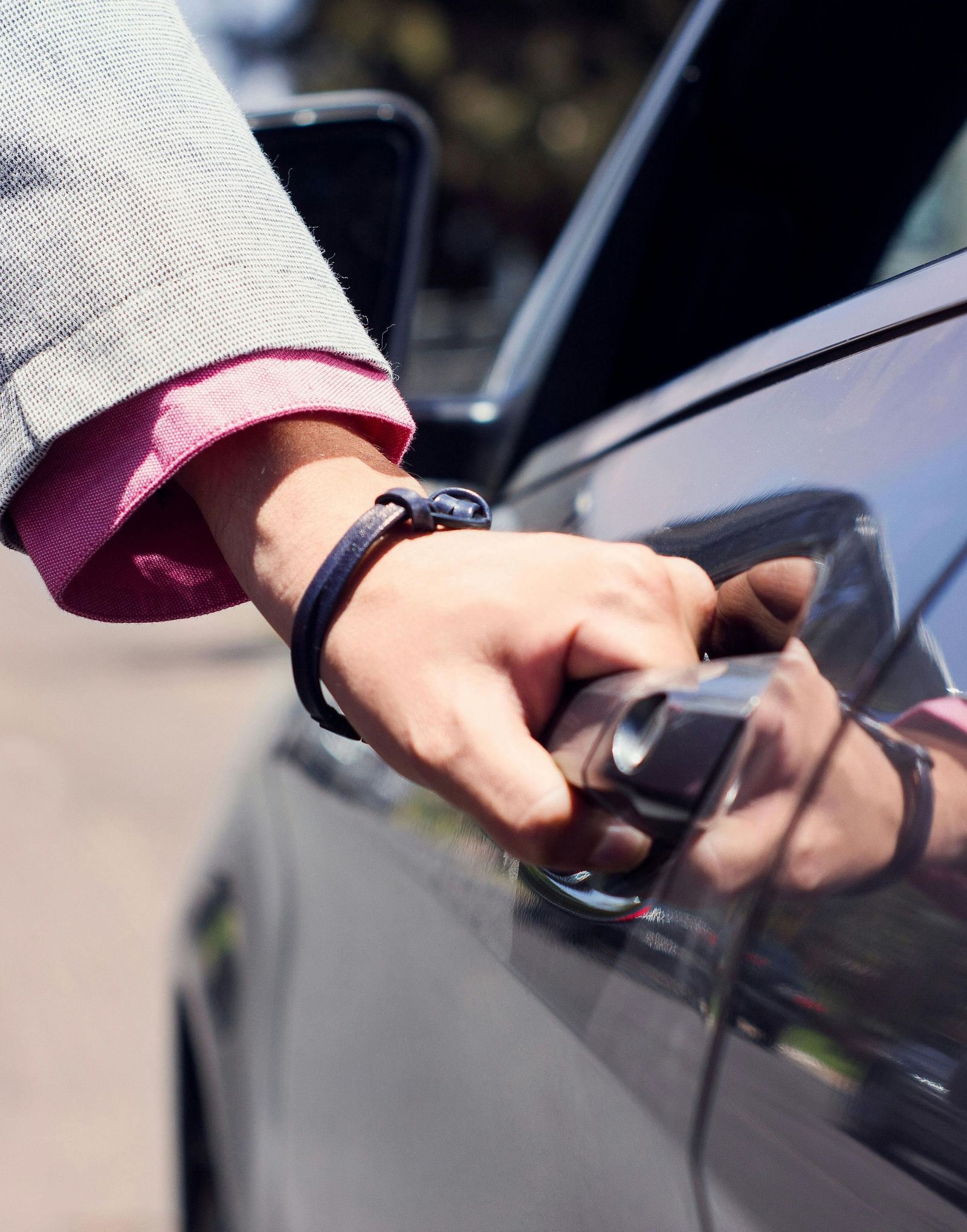 A person dressed in business formals opening the door of a car.