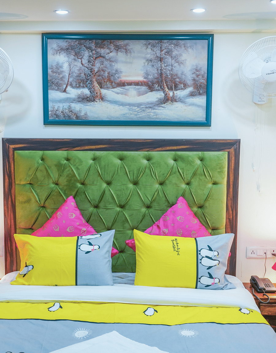 Green tufted headboard with pink and yellow cushions below a snow painting in the Superior King Room, Lime Tree 32nd Avenue