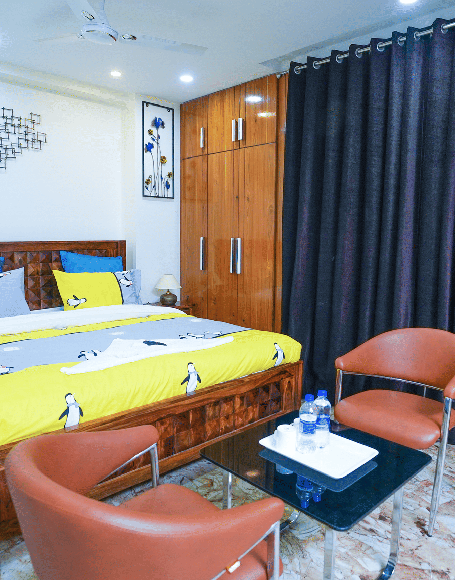 King bed with yellow bedding and two tan leather chairs in the King Room with Balcony at Lime Tree Hotel Near 32nd Avenue