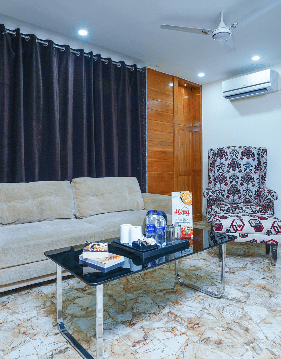Grey sofa, glass coffee table and a patterned wingback chair in the King Room with Balcony, Lime Tree Hotel Near 32nd Avenue