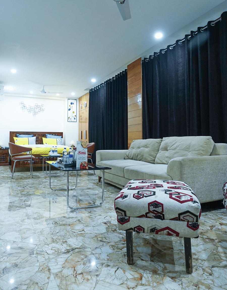 Studio suite at Lime Tree Hotel Near 32nd Avenue with a beige sofa, a wingback chair and a bed with yellow bedding.