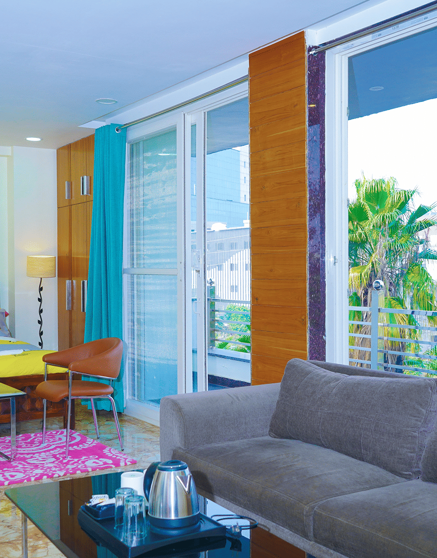 Grey sofa by glass balcony doors with a palm-tree view in the King Room with Balcony, Lime Tree Hotel Near 32nd Avenue