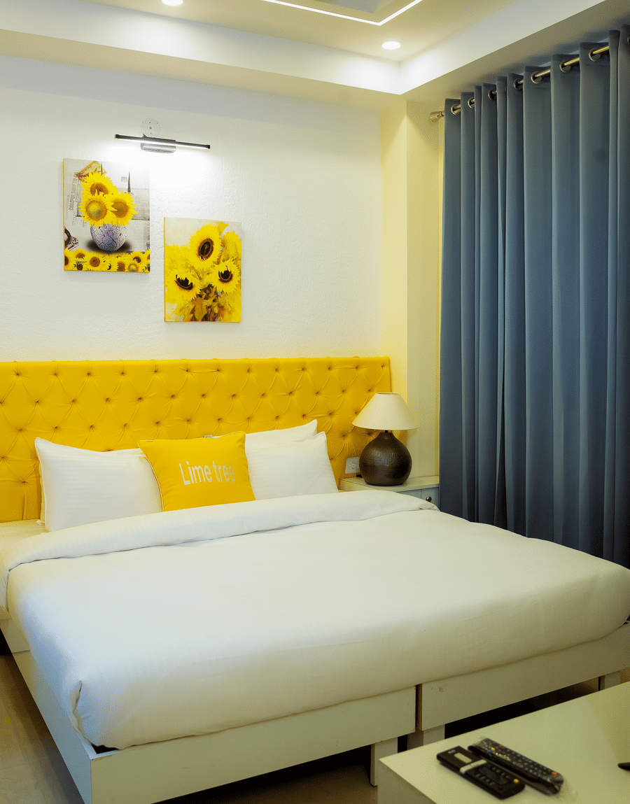 Bed with a yellow tufted headboard and grey curtains in the Standard Studio with Balcony at Lime Tree Luxury Studio