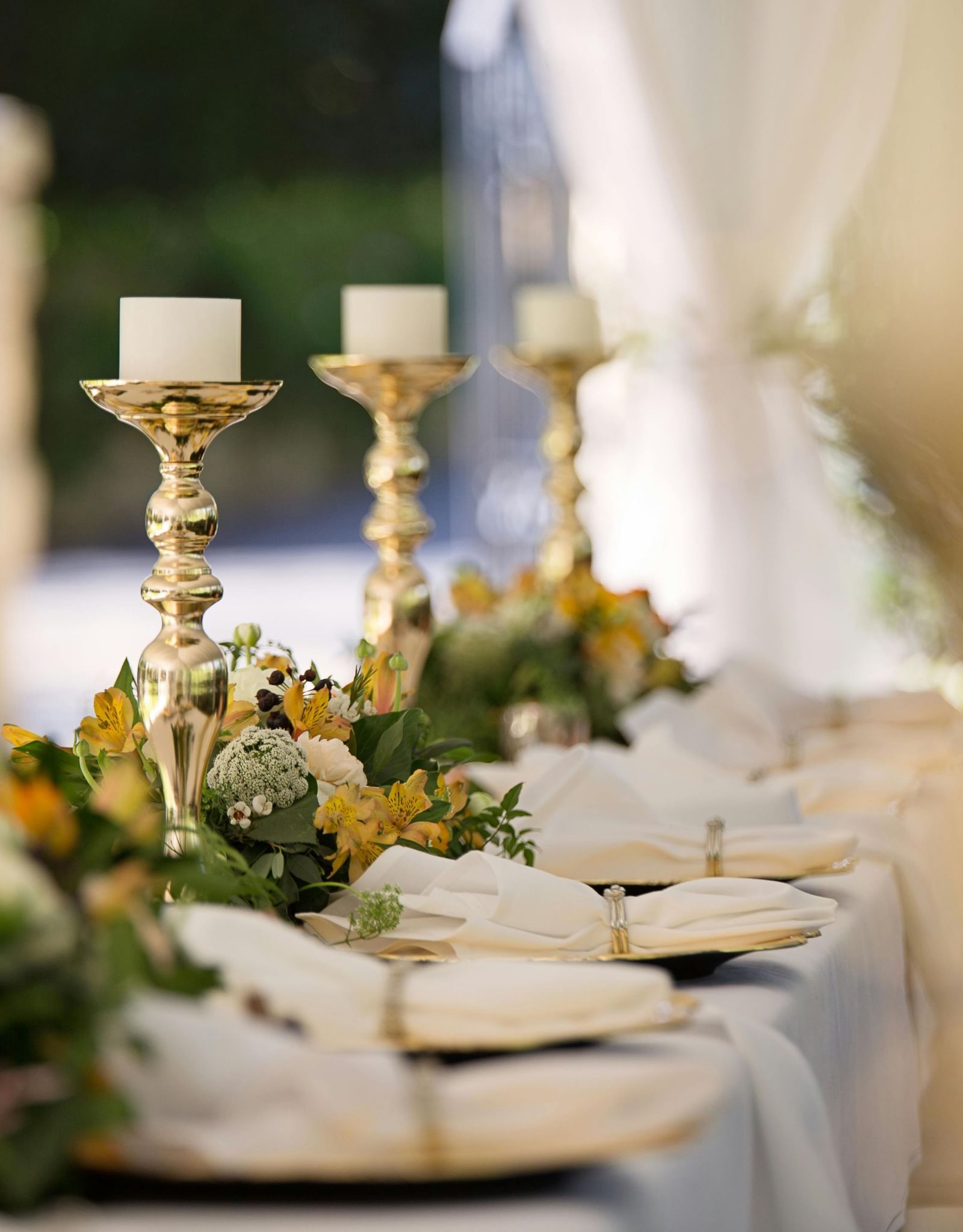 A long table covered with a table cloth decorated with shinny candle stands and well-arranged cutlery.
