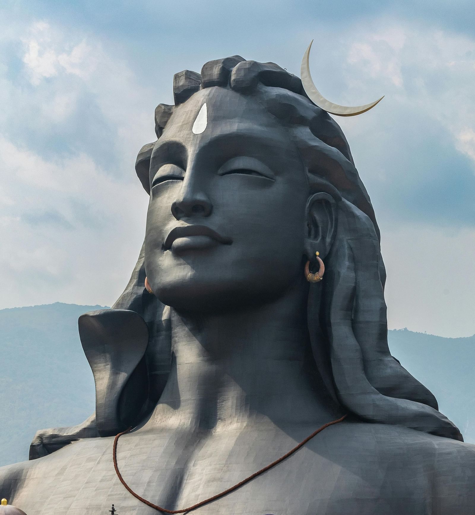 A massive statue of Adiyogi Shiva with the backdrop of mountains and sky