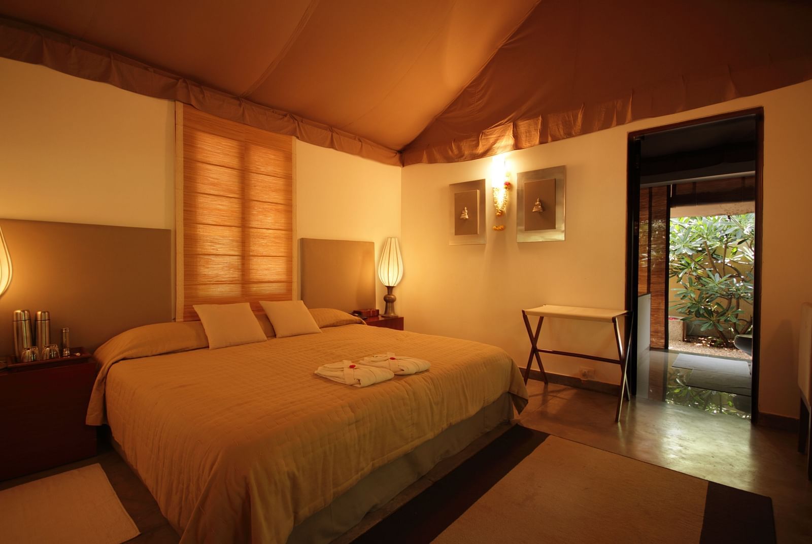 A bedroom with a bed, lamps, and a view of a garden - Shreyas Retreat