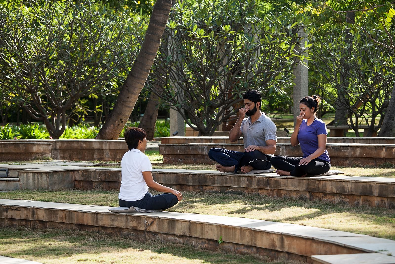 People sitting on steps outdoors, trees, performing yoga - Shreyas Retreat
