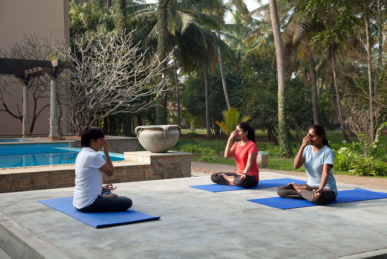 People doing yoga poses on mats by a pool, outdoor setting - Shreyas Retreat
