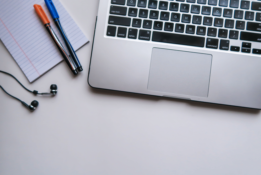 A laptop, a notepad, pens and earphones on a white desk