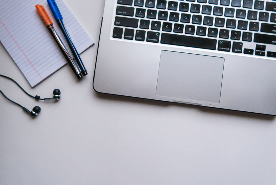 A laptop, a notepad, pens and earphones on a white desk